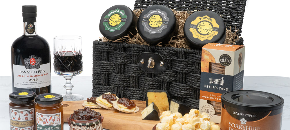 A cheese hamper from The Cheese Wedge Company with a selection of cheese, chutneys, popcorn, crackers and port on display on a wooden board.